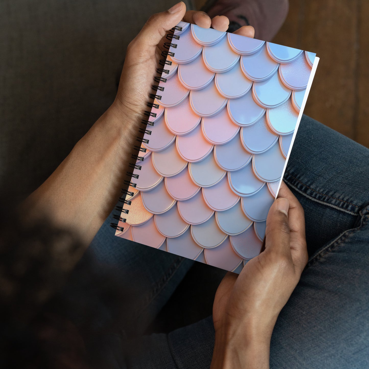 Handheld perspective view of A spiral-bound notebook with a cover illustration of an iridescent mermaid tail pattern.